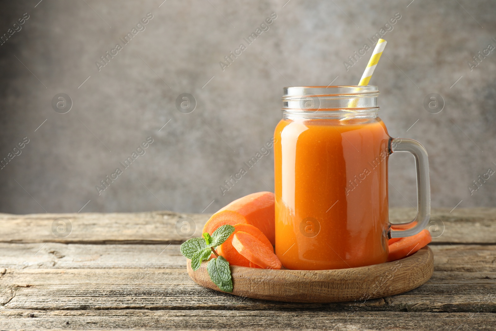 Photo of Fresh carrot juice in mason jar, vegetable and mint on wooden table against gray background, space for text