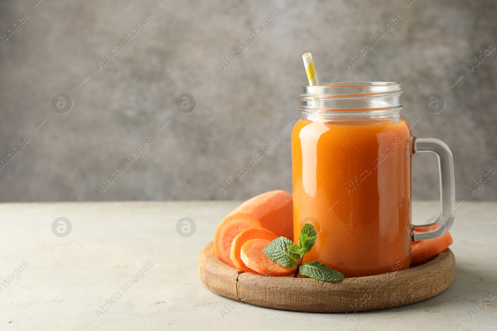 Photo of Fresh carrot juice in mason jar, vegetable and mint on gray textured table, space for text