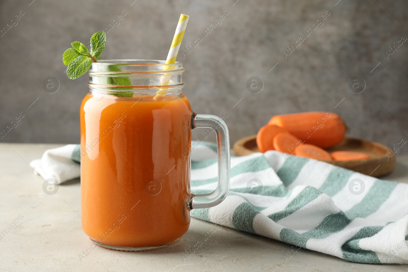 Photo of Fresh carrot juice and mint in mason jar on gray textured table