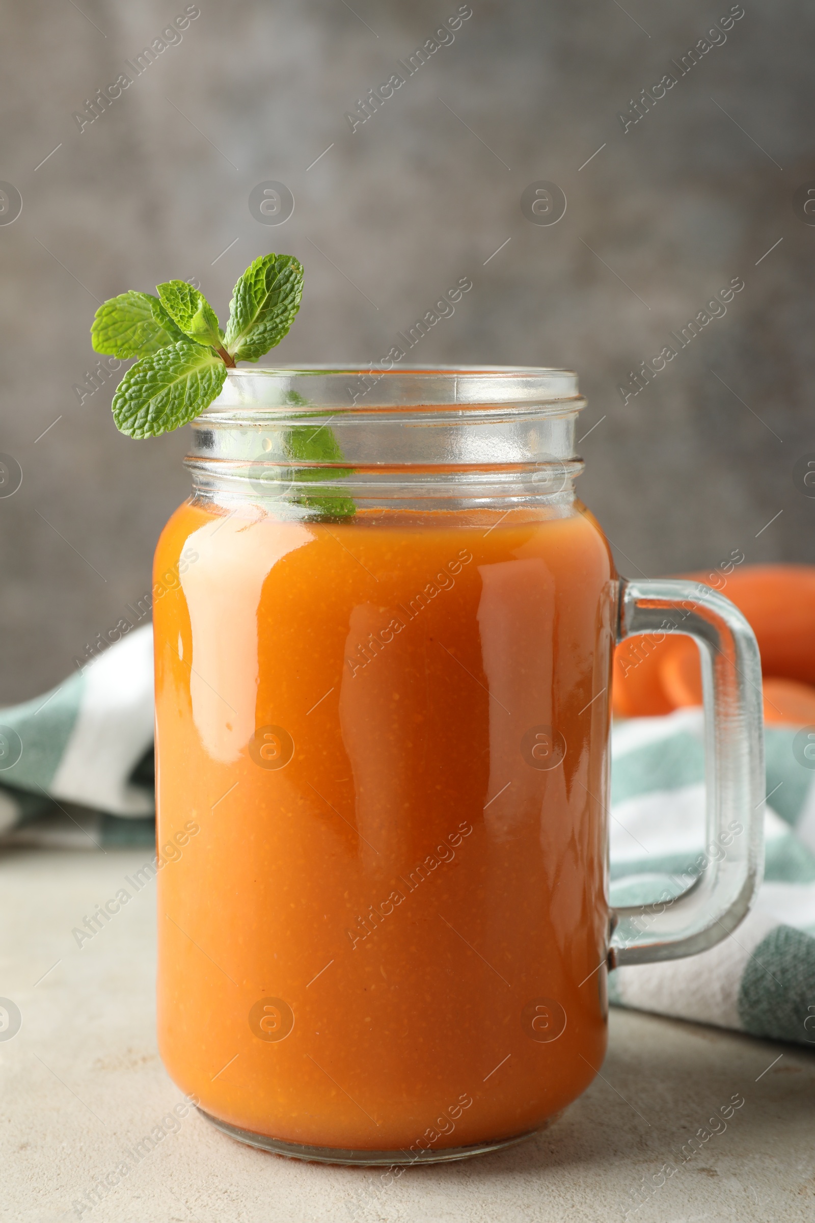 Photo of Fresh carrot juice and mint in mason jar on gray textured table