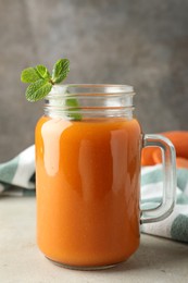 Photo of Fresh carrot juice and mint in mason jar on gray textured table