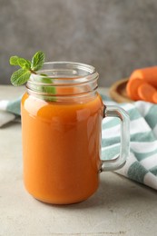 Photo of Fresh carrot juice and mint in mason jar on gray textured table