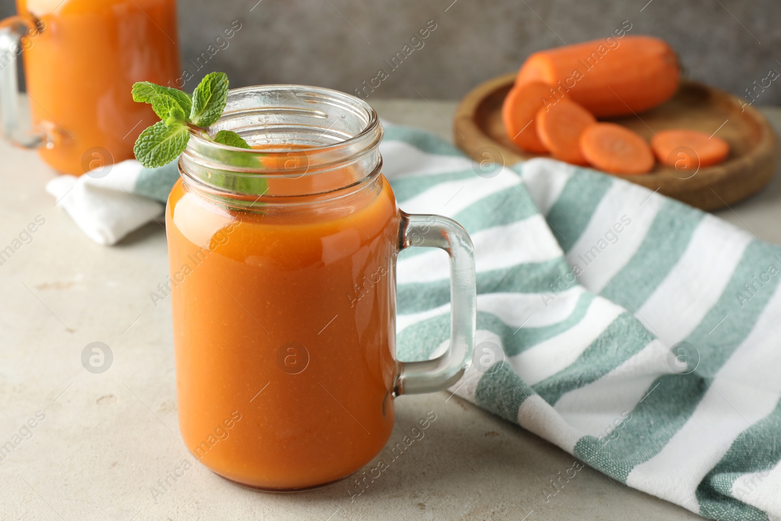 Photo of Fresh carrot juice and mint in mason jar on gray textured table