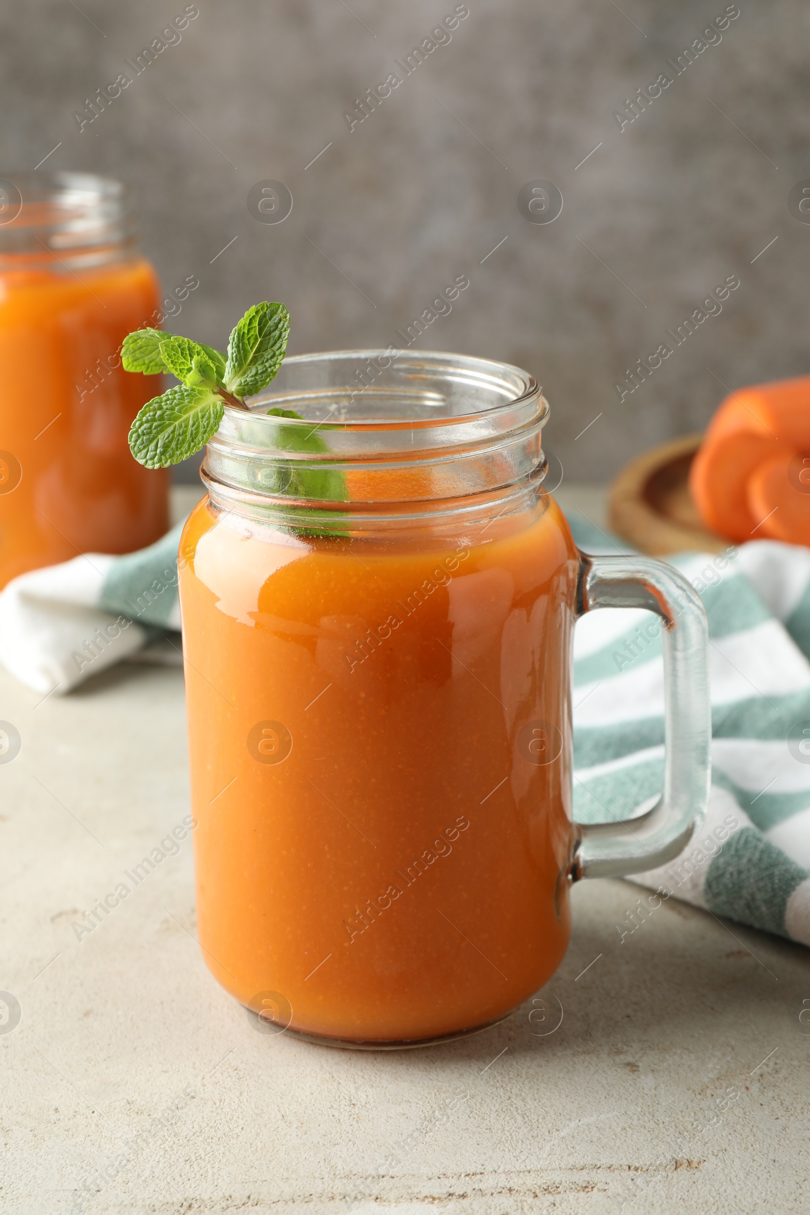 Photo of Fresh carrot juice and mint in mason jar on gray textured table