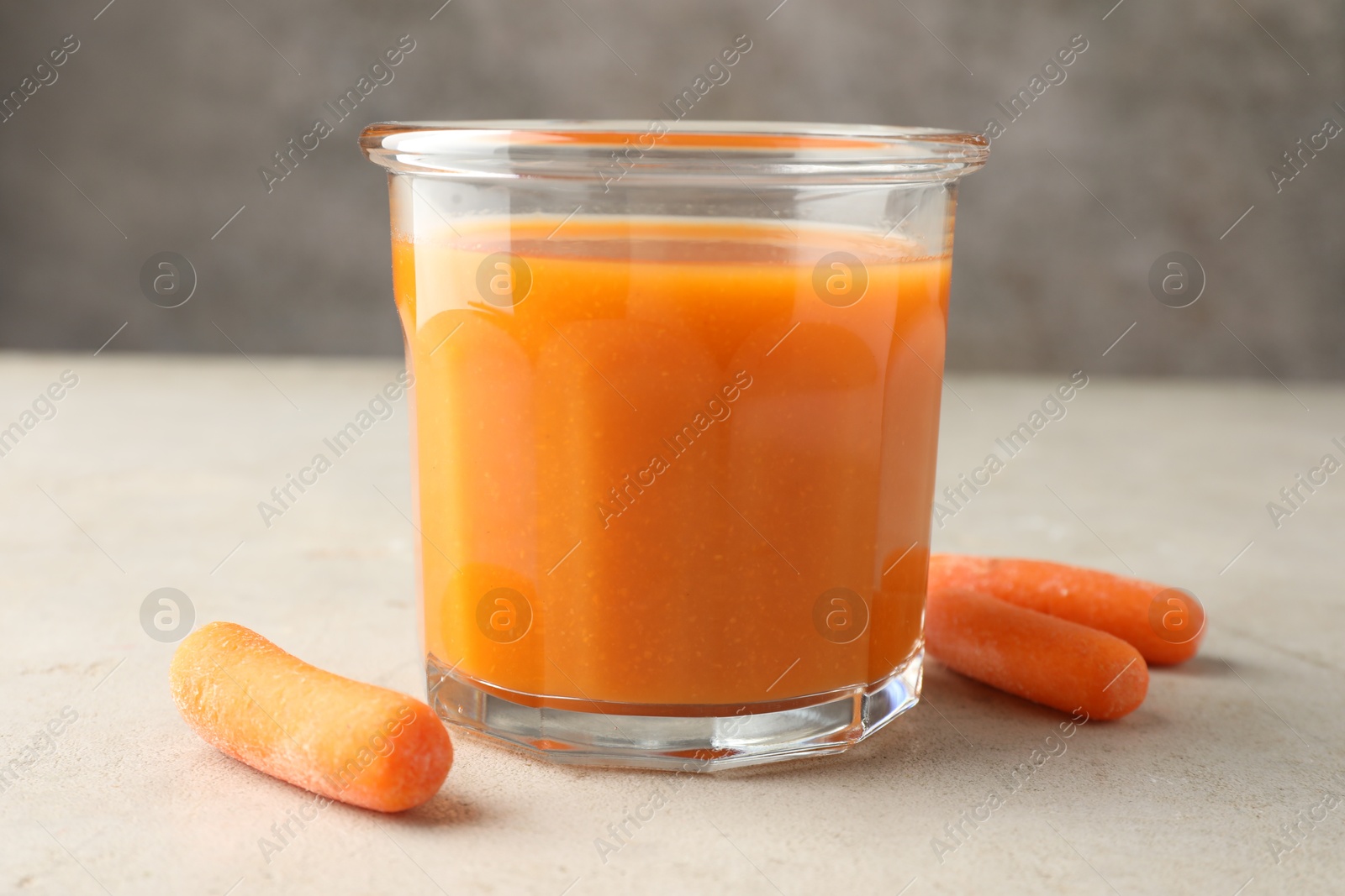 Photo of Fresh carrot juice in glass and vegetables on gray textured table, closeup