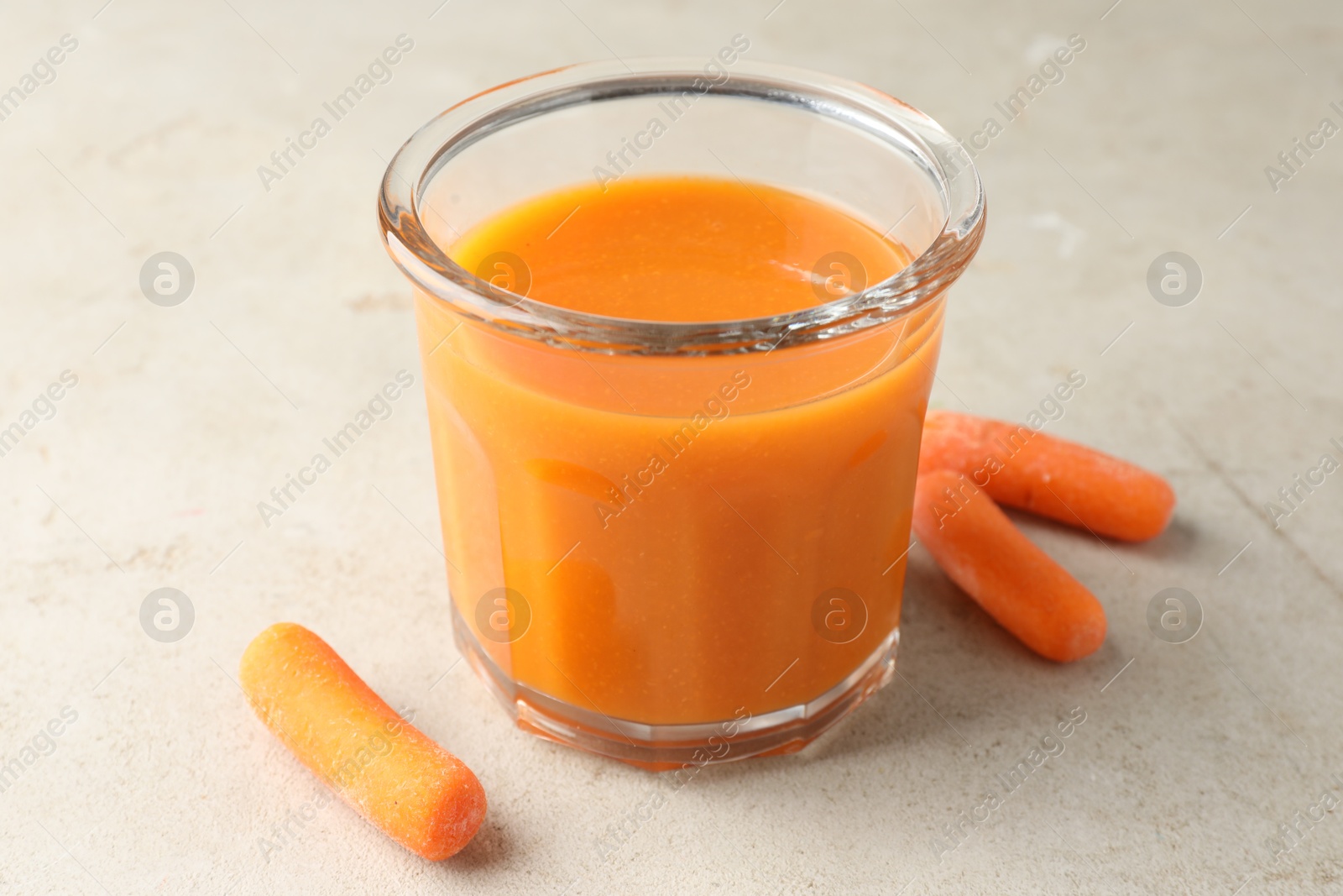 Photo of Fresh carrot juice in glass and vegetables on gray textured table