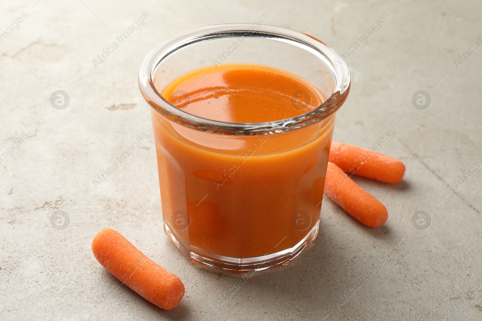 Photo of Fresh carrot juice in glass and vegetables on gray textured table