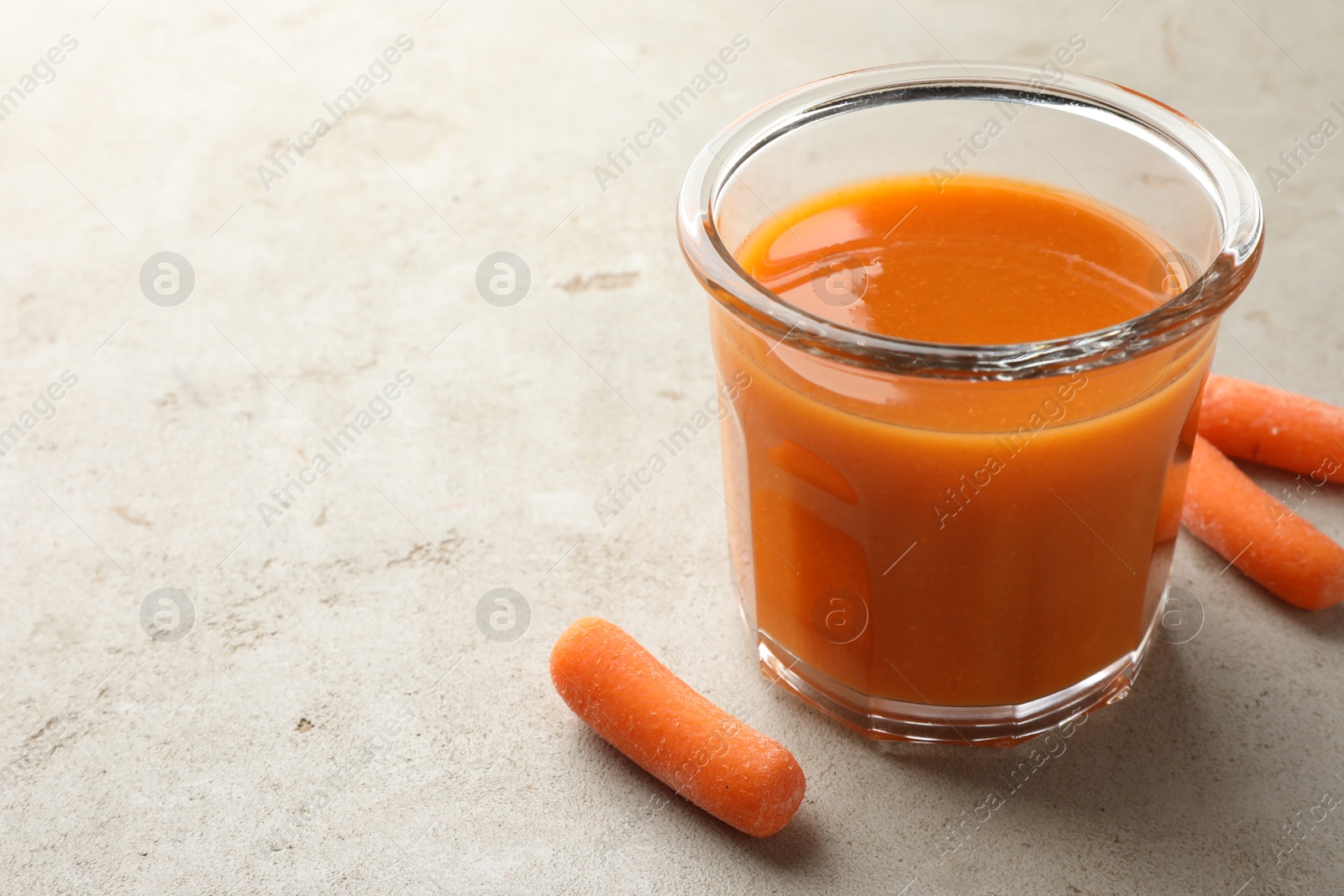 Photo of Fresh carrot juice in glass and vegetables on gray textured table, space for text