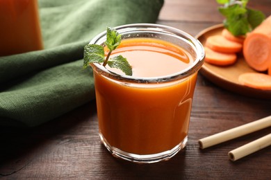 Photo of Fresh carrot juice in glass, vegetables, mint and straws on wooden table