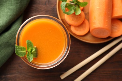 Photo of Fresh carrot juice in glass, vegetables, mint and straws on wooden table, flat lay