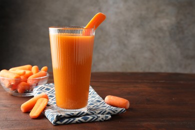 Photo of Fresh carrot juice in glass and vegetables on wooden table against gray background, space for text