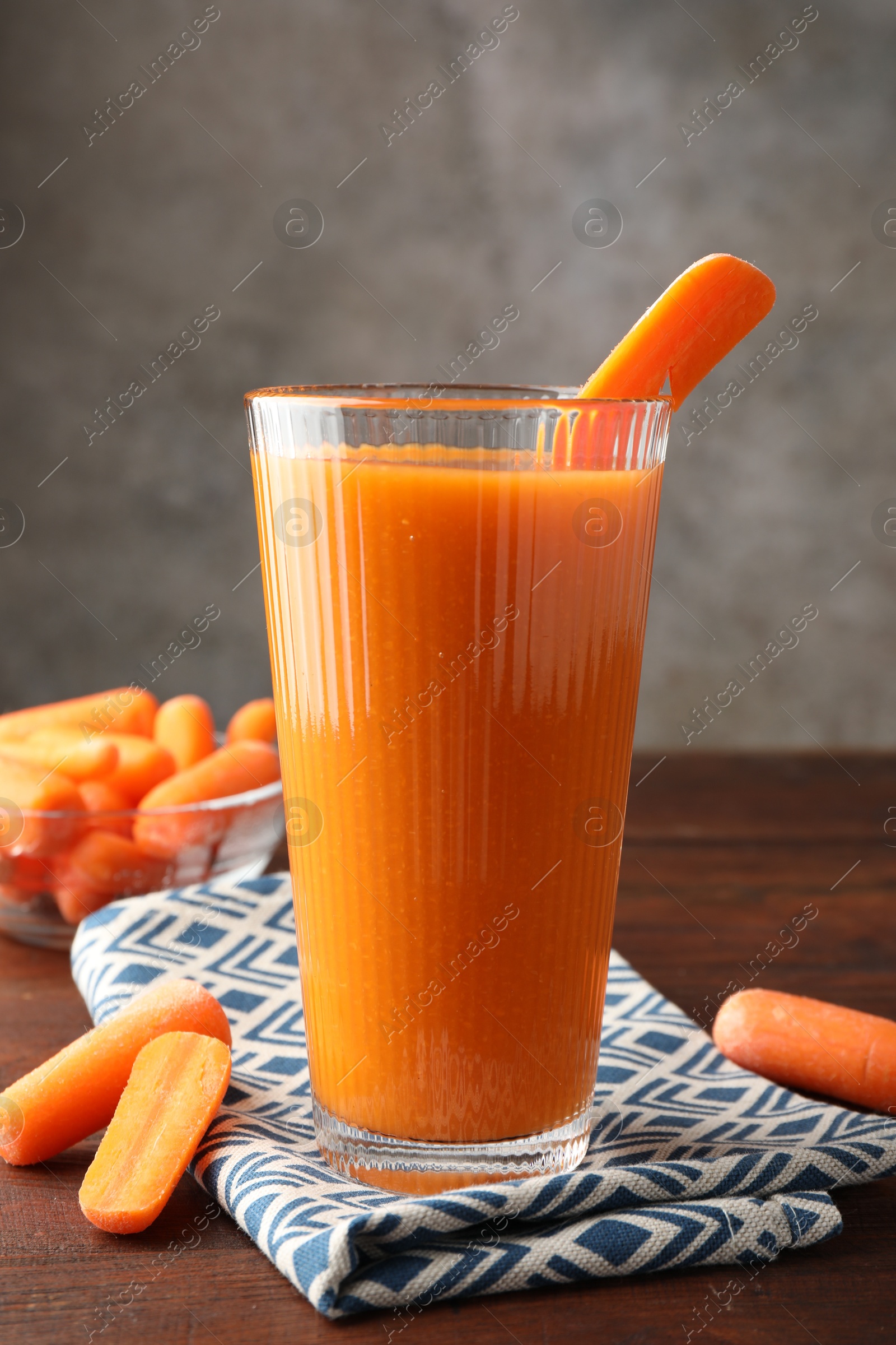 Photo of Fresh carrot juice in glass and vegetables on wooden table against gray background