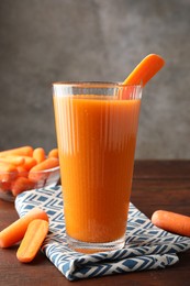 Photo of Fresh carrot juice in glass and vegetables on wooden table against gray background