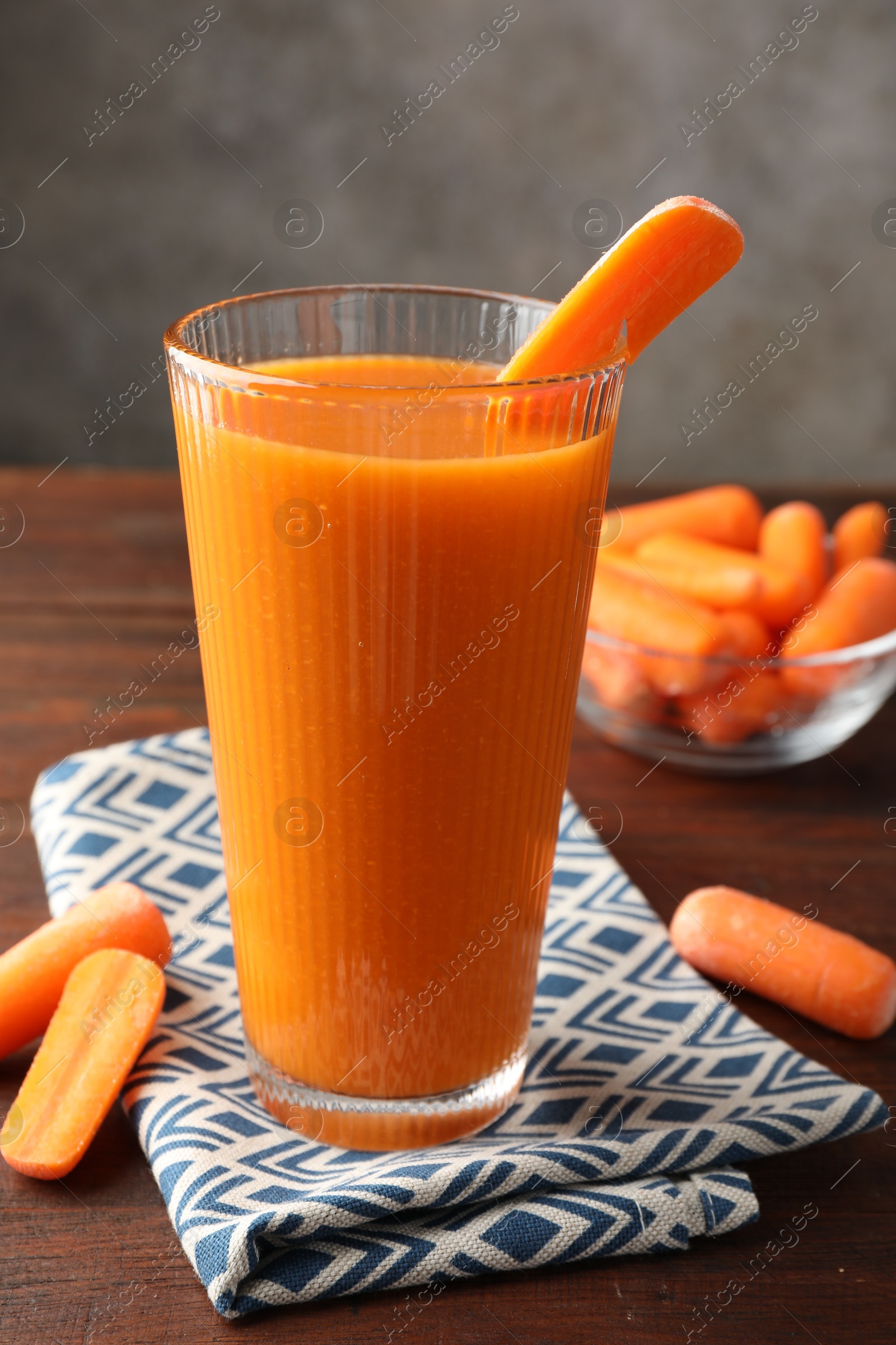 Photo of Fresh carrot juice in glass and vegetables on wooden table against gray background