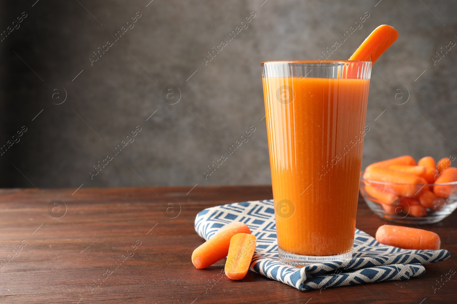 Photo of Fresh carrot juice in glass and vegetables on wooden table against gray background, space for text