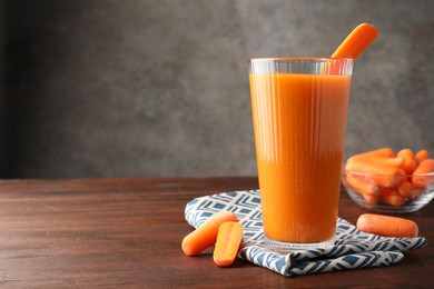 Photo of Fresh carrot juice in glass and vegetables on wooden table against gray background, space for text