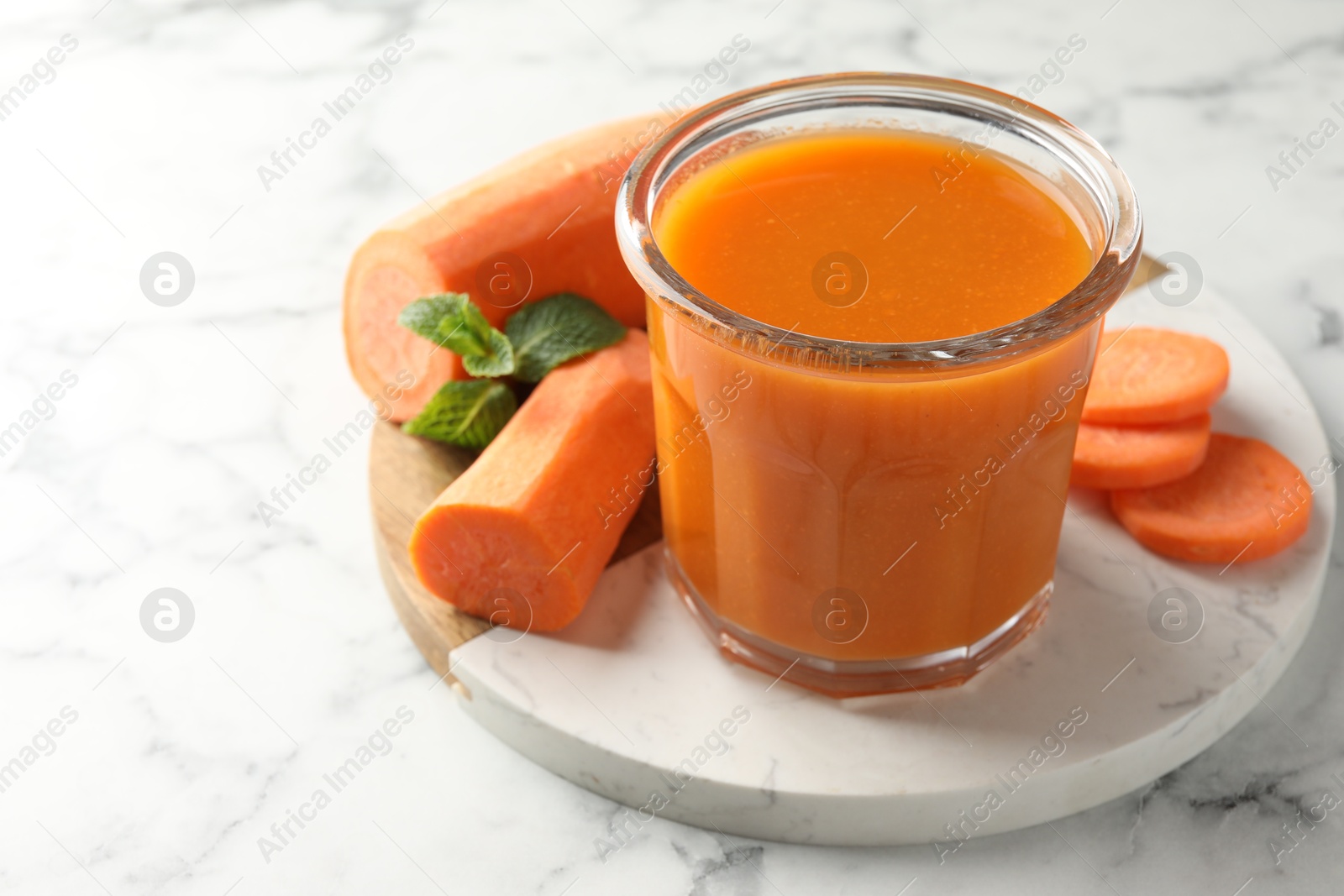 Photo of Fresh carrot juice in glass, vegetables and mint on white marble table, closeup