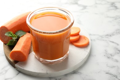 Photo of Fresh carrot juice in glass, vegetables and mint on white marble table, closeup