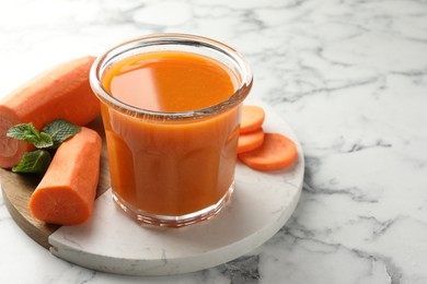 Photo of Fresh carrot juice in glass, vegetables and mint on white marble table, closeup