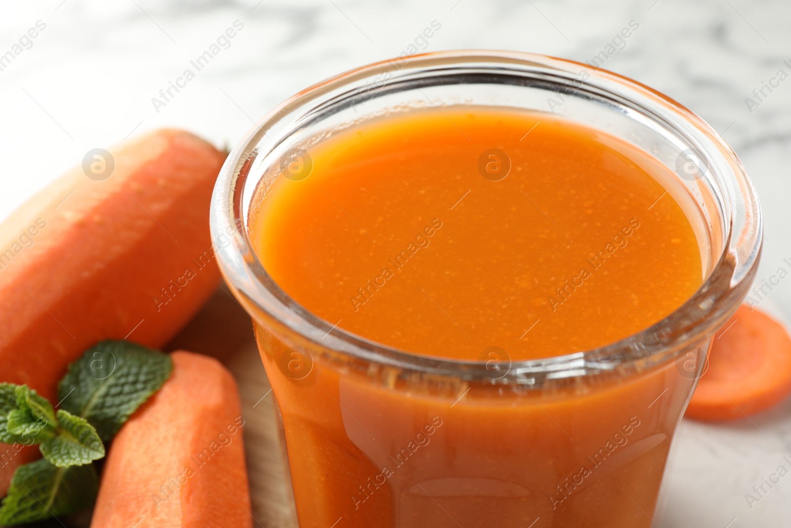 Photo of Fresh carrot juice in glass, vegetables and mint on light table, closeup