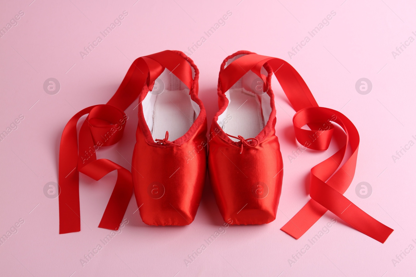 Photo of Pair of beautiful red pointe shoes on pink background