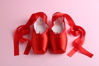 Photo of Pair of beautiful red pointe shoes on pink background