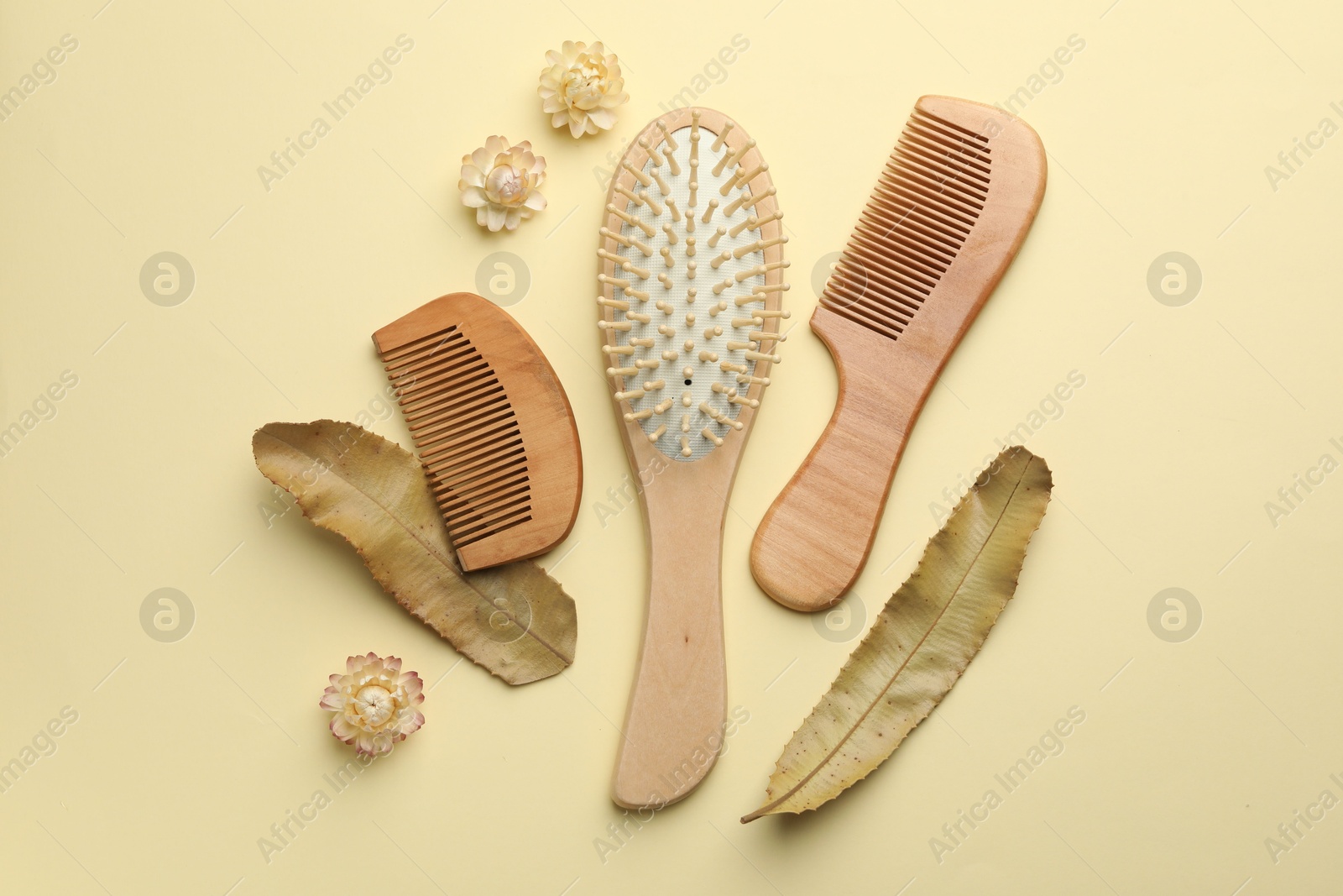 Photo of Wooden hair brush, combs, flowers and leaves on beige background, flat lay