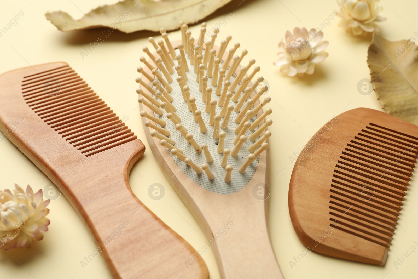 Photo of Wooden hair brush, combs, flowers and leaves on beige background, closeup