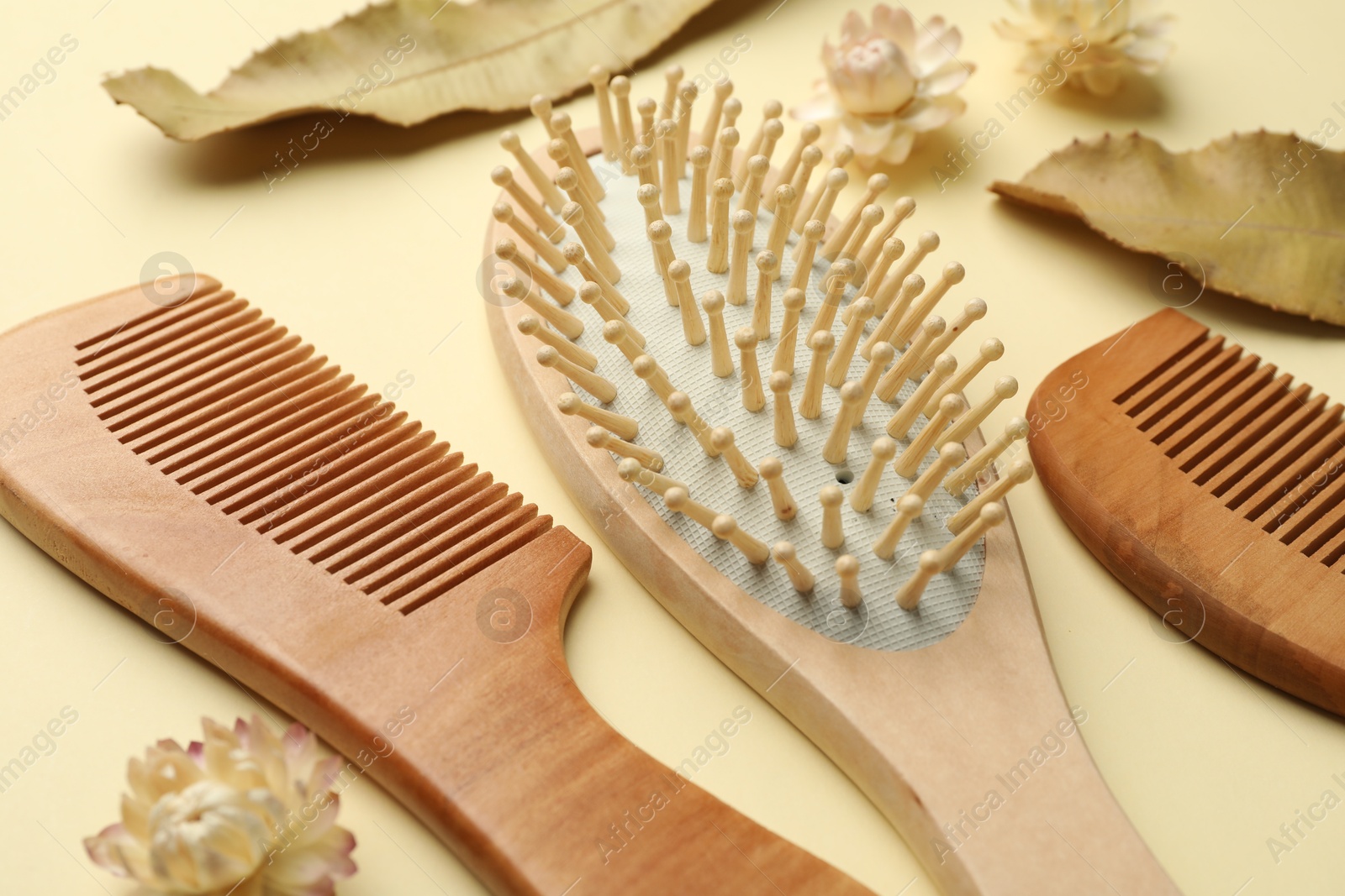 Photo of Wooden hair brush, combs, flowers and leaves on beige background, closeup