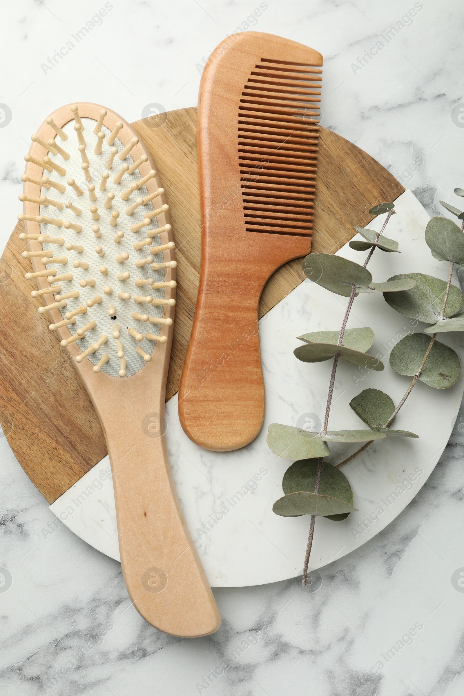 Photo of Hair brush, comb and eucalyptus on white marble background, top view