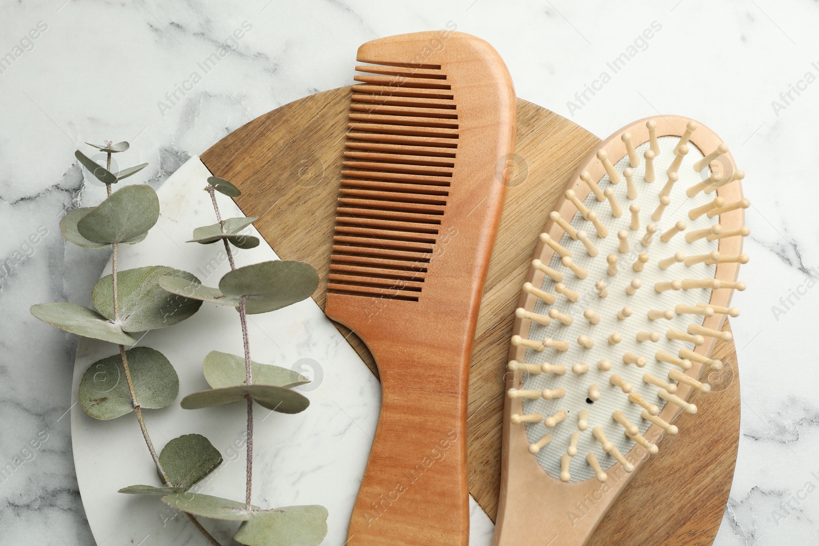 Photo of Hair brush, comb and eucalyptus on white marble background, top view