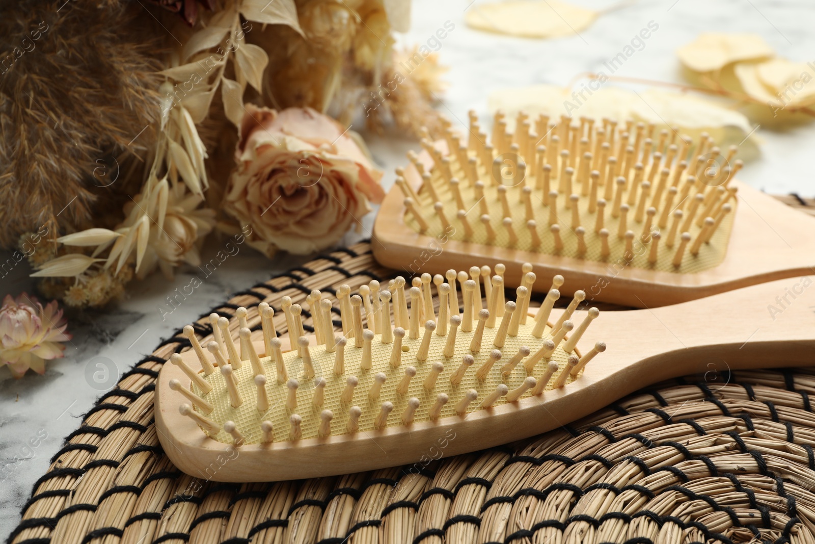 Photo of Wooden hair brushes and dried flowers on white marble background, closeup