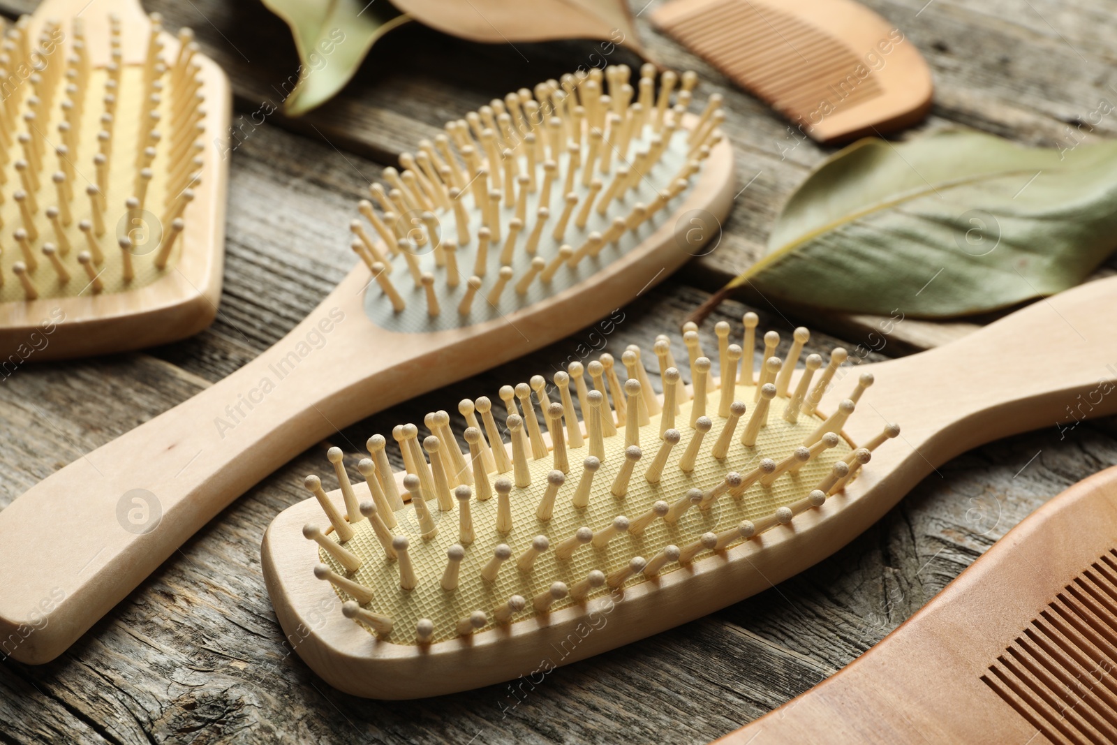 Photo of Hair brushes, combs and leaves on wooden background, closeup