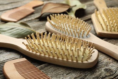 Photo of Hair brushes, combs and leaves on wooden background, closeup