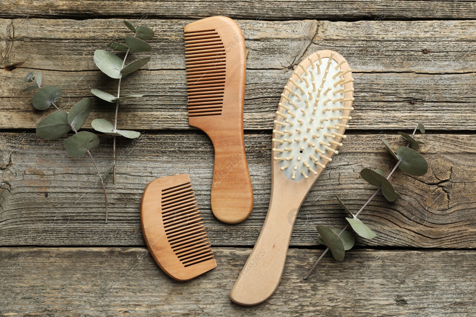 Photo of Hair brush, combs and eucalyptus on wooden background, flat lay