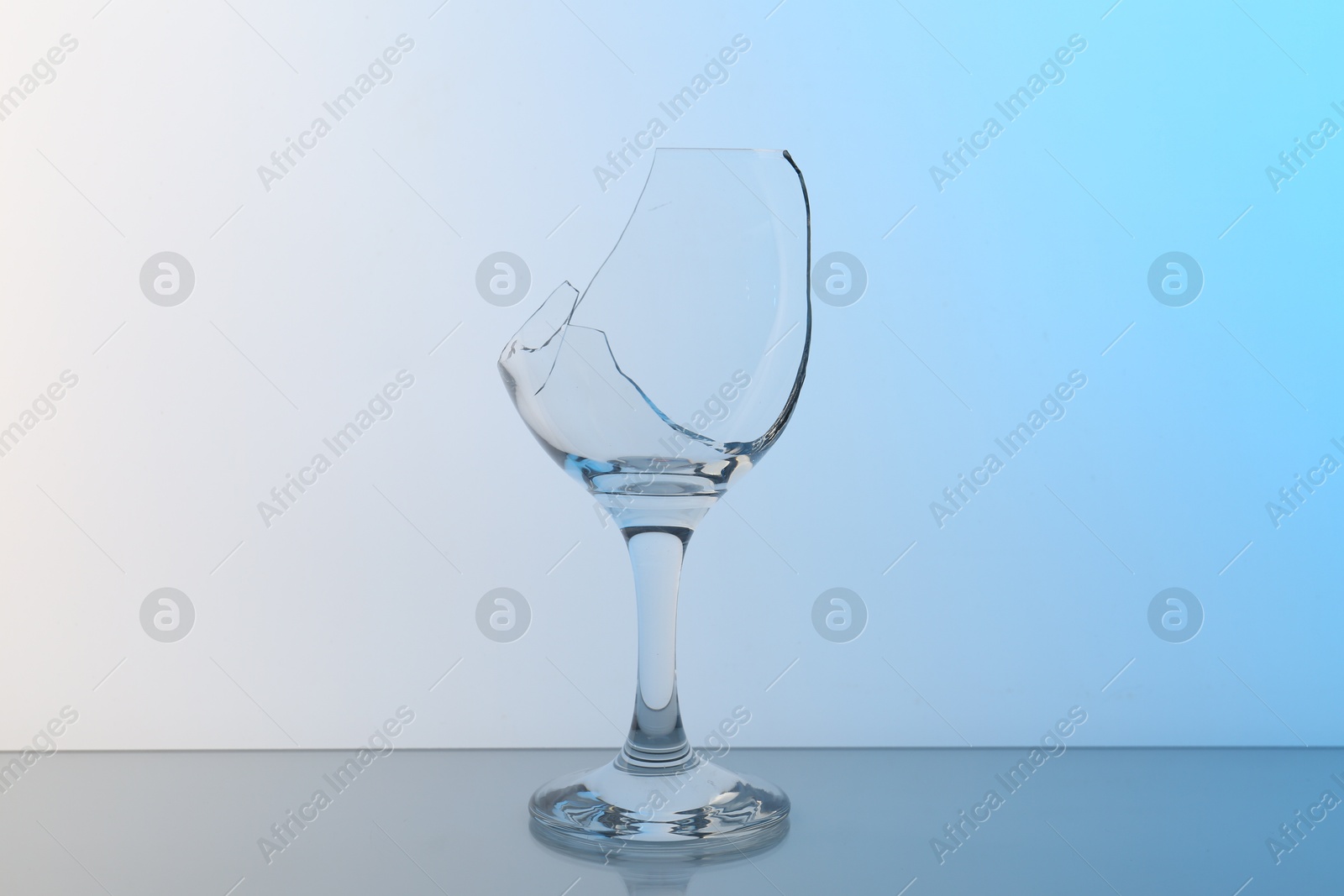 Photo of Broken wine glass on table against light blue gradient background