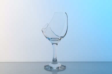 Photo of Broken wine glass on table against light blue gradient background