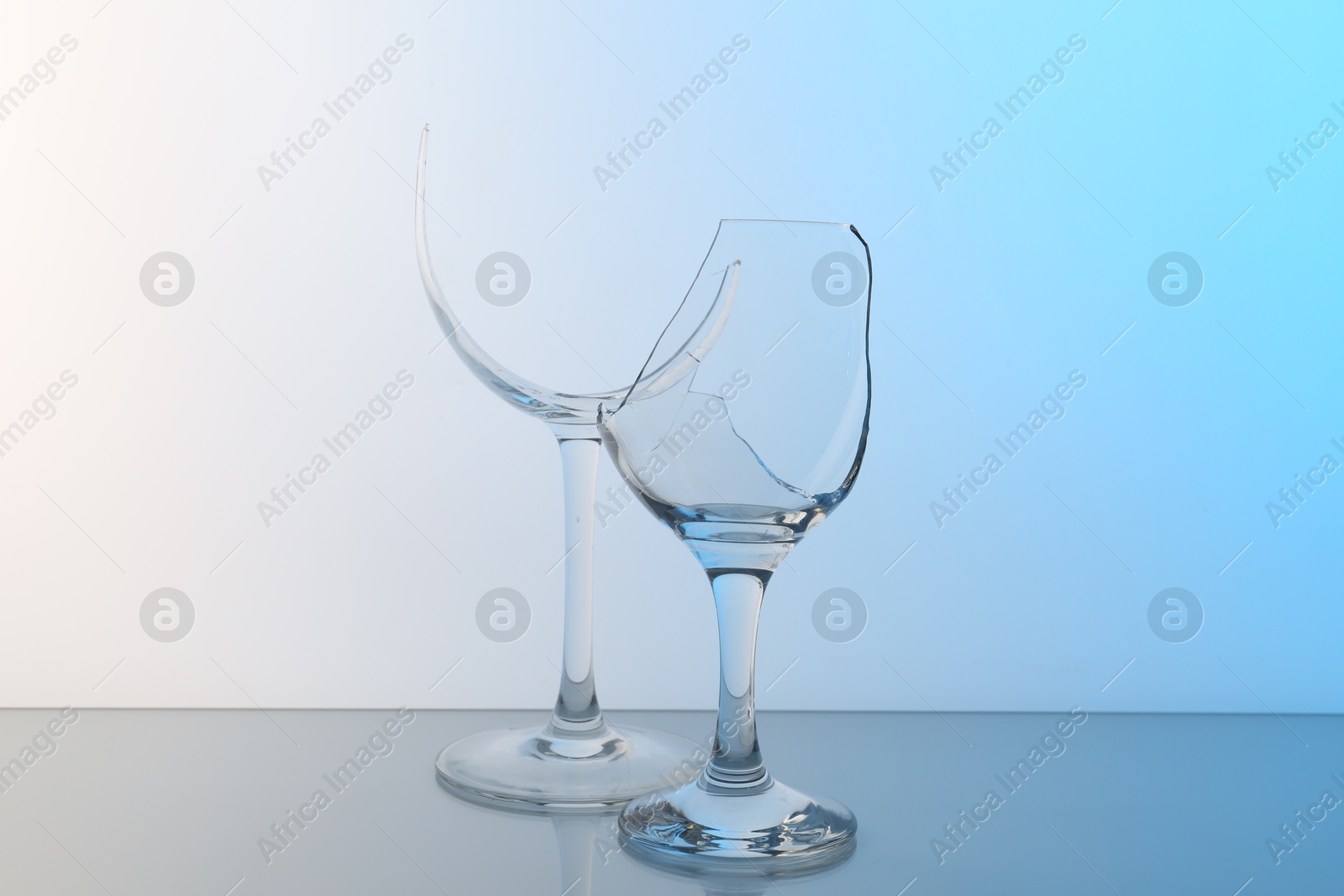 Photo of Broken wine glasses on table against light blue gradient background