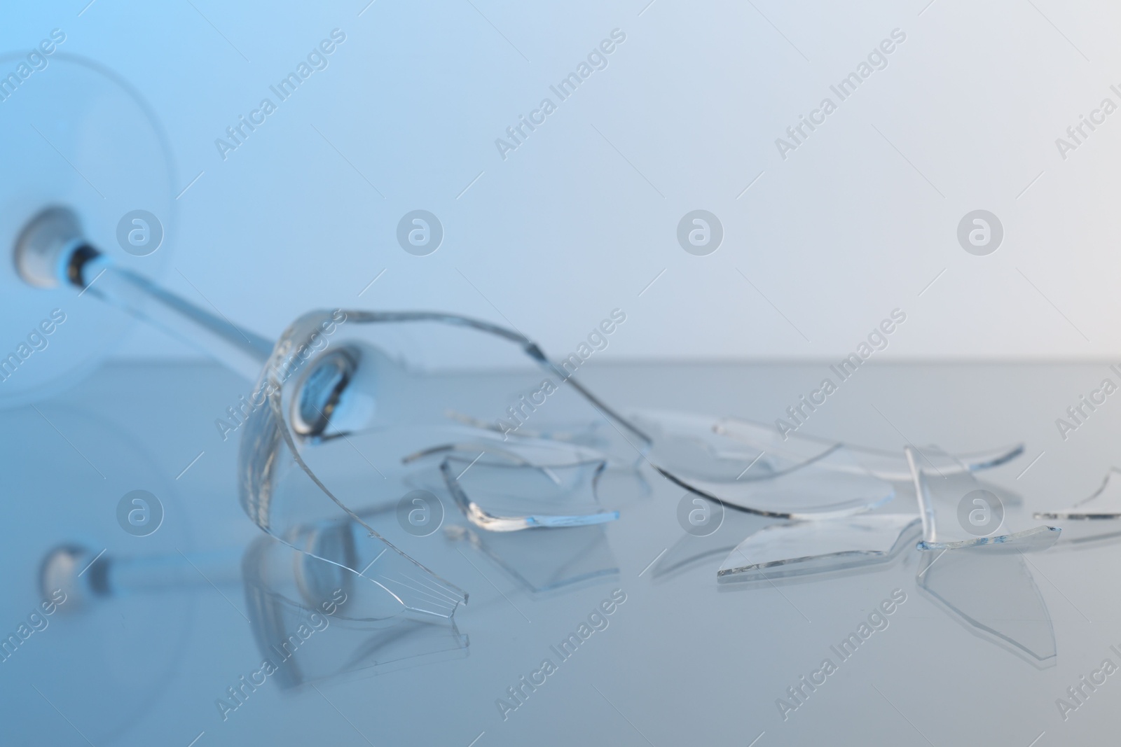 Photo of Pieces of broken wine glass on table against light blue gradient background, closeup