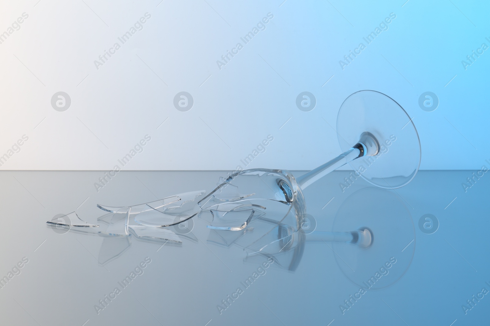 Photo of Pieces of broken wine glass on table against light blue gradient background