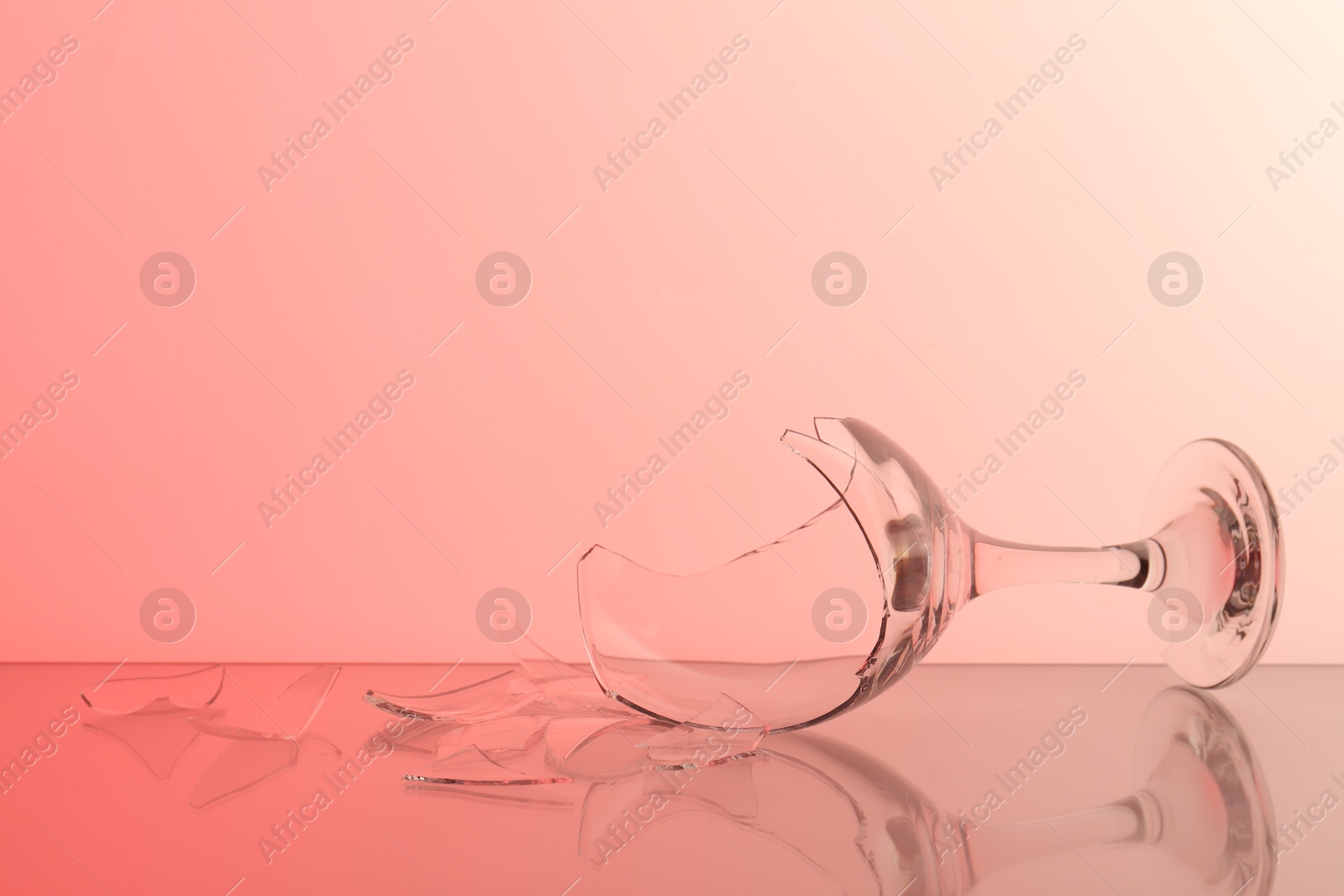 Photo of Pieces of broken wine glass on table against color background