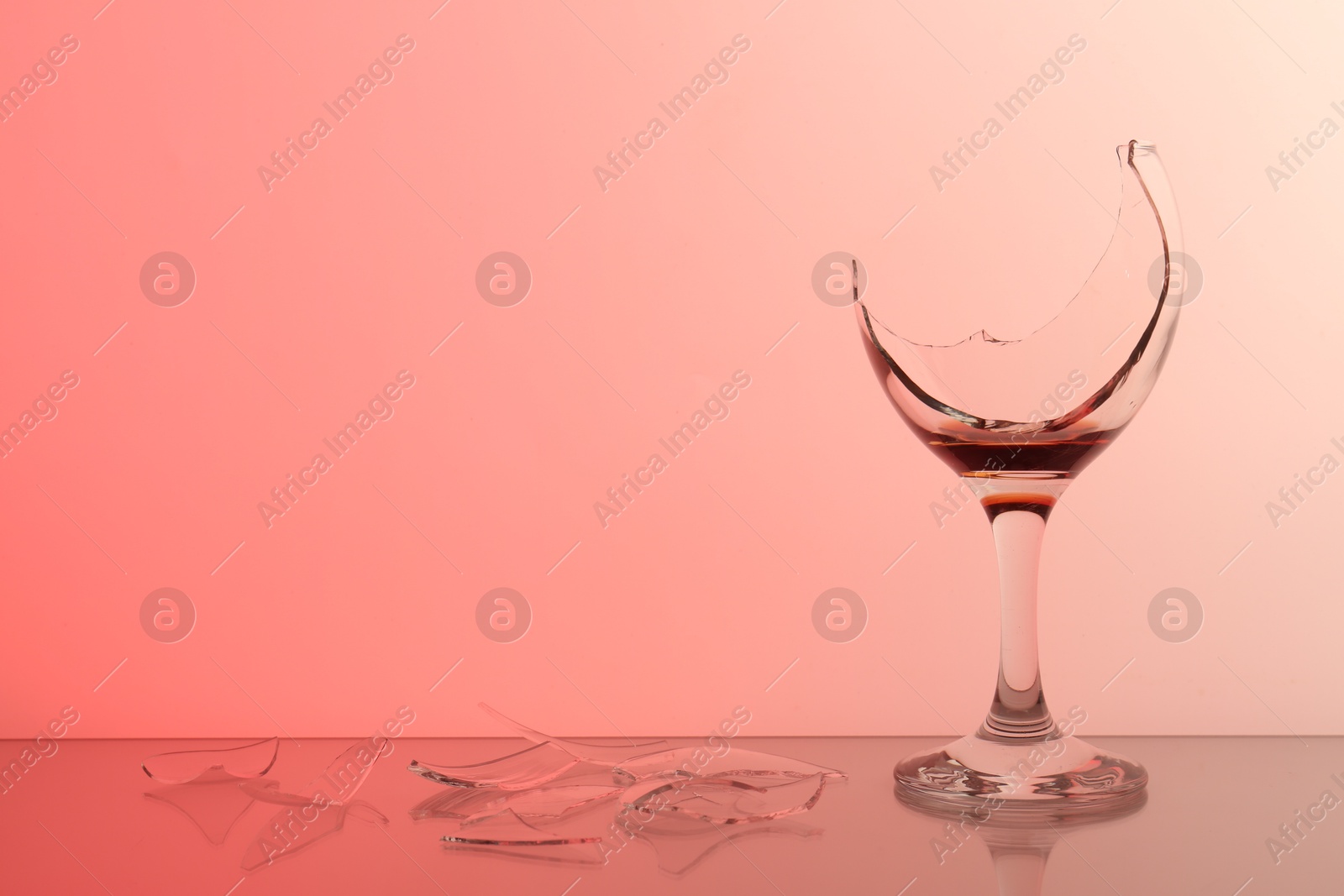 Photo of Pieces of broken glass with wine on table against color background, space for text