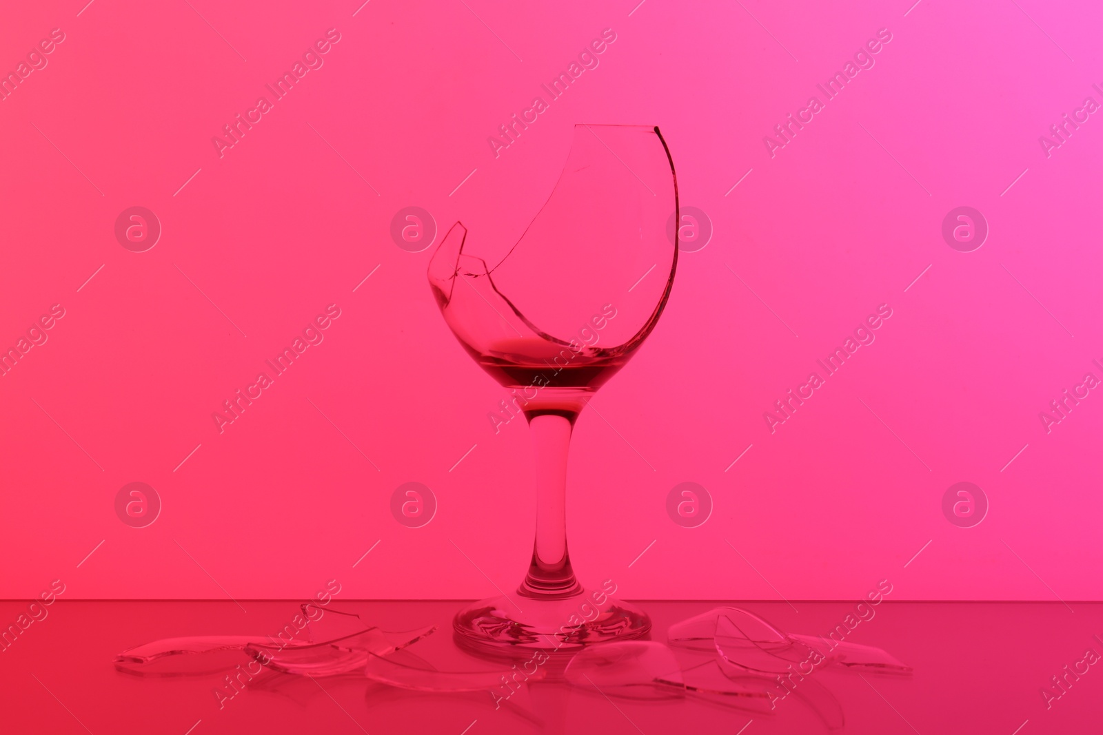 Photo of Pieces of broken glass with wine against hot pink background, color tone effect