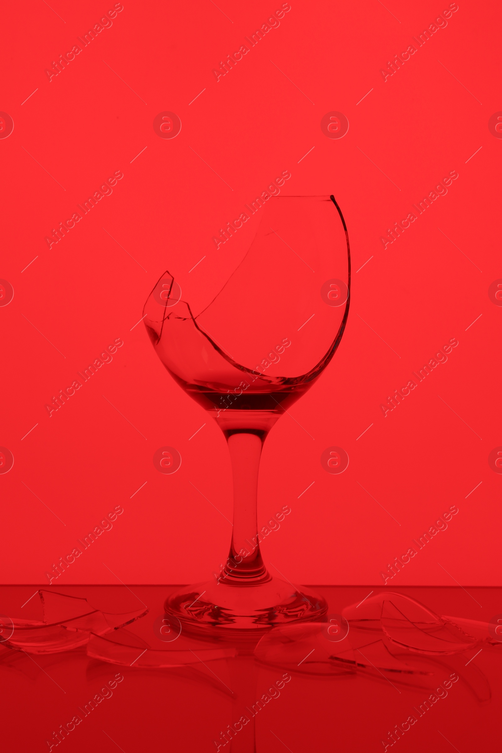 Photo of Pieces of broken glass with wine against red background, color tone effect