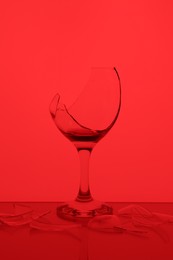 Photo of Pieces of broken glass with wine against red background, color tone effect