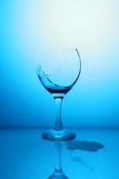 Photo of Broken glass with spilled wine against light blue gradient background