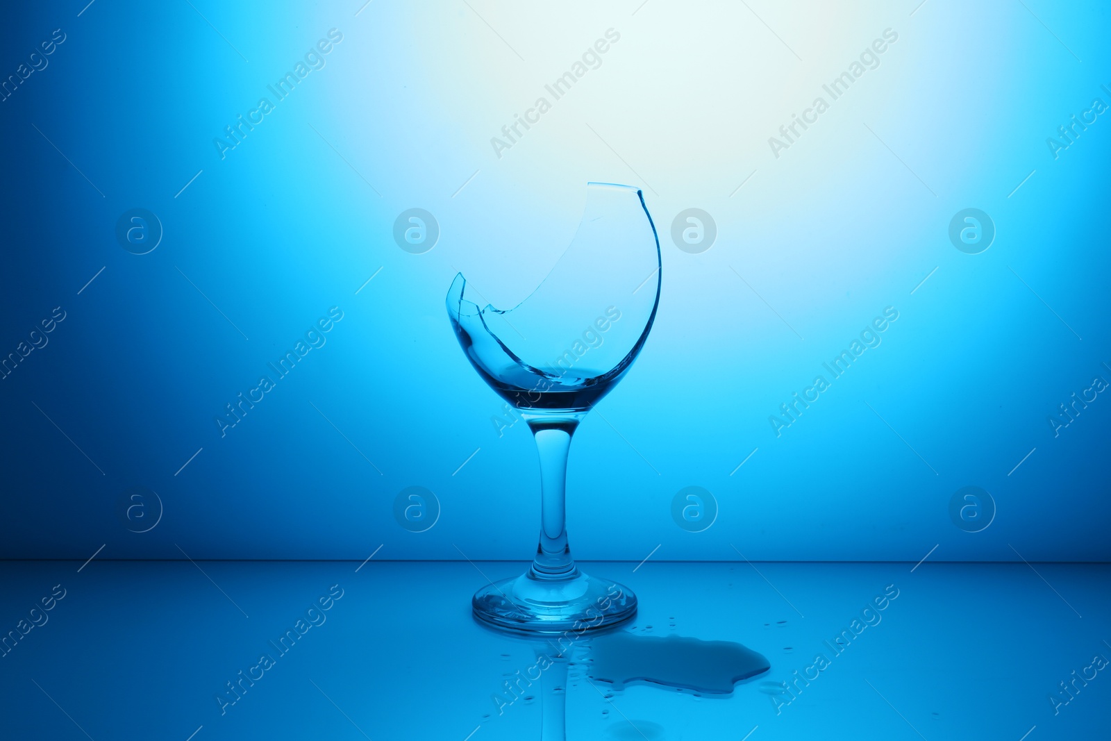 Photo of Broken glass with spilled wine against light blue gradient background