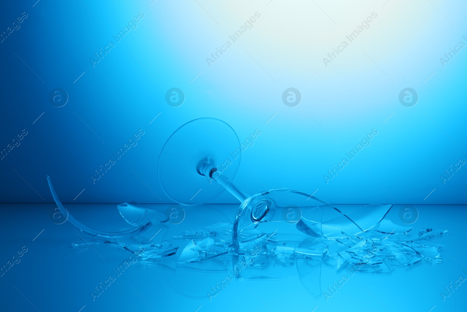 Photo of Pieces of broken wine glass against light blue gradient background