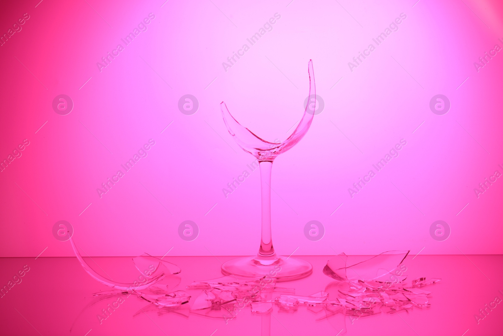 Photo of Pieces of broken wine glass against magenta gradient background, color tone effect