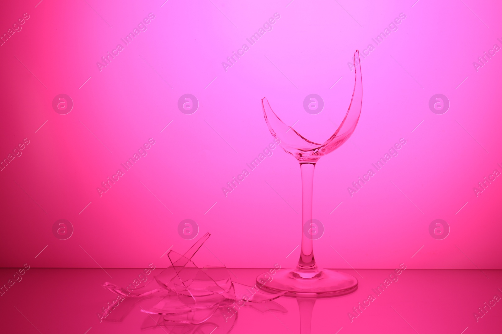 Photo of Pieces of broken wine glass against magenta gradient background, color tone effect